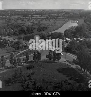 An archival high-angle panorama from July 1997, showing the embankment area of the Torets River in Sloviansk, Ukraine. The view captures a busy road bridge with car traffic crossing the river on the left, and a road intersection below. The winding river flows through a landscape of dense green trees. In the distance, a second, arched bridge is visible. This photo shows the city landscape in the post-Soviet 1990s. This is a moment of everyday life in the peaceful Donbas before the war. Stock Photo