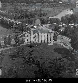 An archival high-angle panorama from July 1997, showing the embankment area of the Torets River in Sloviansk, Ukraine. The view captures a busy road bridge with car traffic crossing the river on the left, and a road intersection below. The winding river flows through a landscape of dense green trees. In the distance, a second, arched bridge is visible. This photo shows the city landscape in the post-Soviet 1990s. This is a moment of everyday life in the peaceful Donbas before the war. Stock Photo