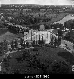 An archival high-angle panorama from July 1997, showing the embankment area of the Torets River in Sloviansk, Ukraine. The view captures a busy road bridge with car traffic crossing the river on the left, and a road intersection below. The winding river flows through a landscape of dense green trees. In the distance, a second, arched bridge is visible. This photo shows the city landscape in the post-Soviet 1990s. This is a moment of everyday life in the peaceful Donbas before the war. Stock Photo