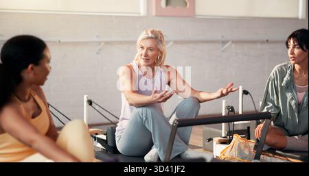 Pilates, talking and women on machine in gym for fitness advice, workout tips and exercise. Health club, trainer and friends in discussion, chat or Stock Photo
