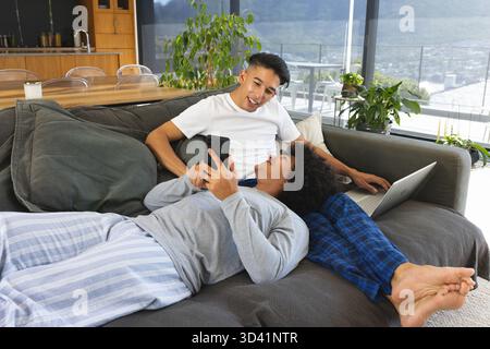 Two men lounging on gray sofa in modern apartment living room, with smartphone and laptop Stock Photo
