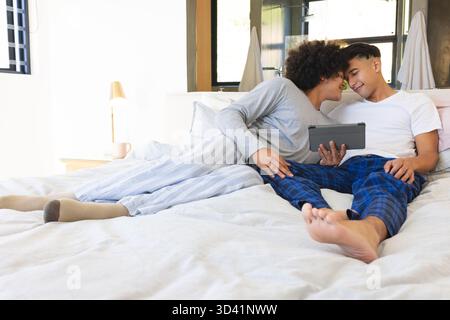 Relaxing together two men sharing tablet on bed in bright modern bedroom, with pillows and blanket Stock Photo