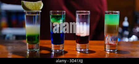 Vibrant layers of colorful shots display a creative mixology masterpiece. Each glass captures light beautifully while showcasing a spectrum of colors, igniting excitement in lively bar atmosphere. Stock Photo