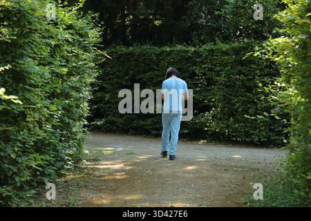Young man walking on garden path surrounded by green bushes Stock Photo