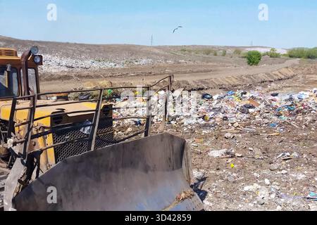 A bulldozer clears heaps of garbage in a garbage can. Work bulldozer in a landfill. Garbage dump, top view of the trash. Landfill. Stock Photo