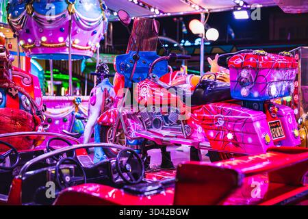 Milan, italy 27 october 2025: amusement park carousel features vibrant motorcycle and hot air balloon rides under bright neon lights, creating a festi Stock Photo