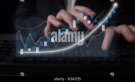 Close-up of hands typing on a keyboard with overlaid digital charts displaying financial data, showcasing investment trends and performance analysis Stock Photo