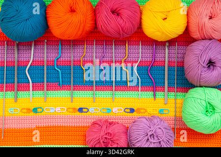 All for hand knitting. Knitted multi-colored handmade fabric with balls of multi-colored threads, pins and various knitting needles on it. Stock Photo