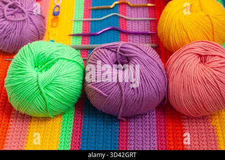 All for hand knitting. Knitted multi-colored handmade fabric with balls of multi-colored threads, pins and various knitting needles on it. Stock Photo