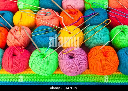 All for hand knitting. Knitted multi-colored handmade fabric with balls of multi-colored threads, pins and various knitting needles on it. Stock Photo