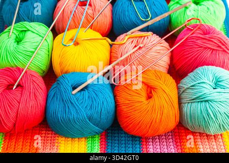 All for hand knitting. Knitted multi-colored handmade fabric with balls of multi-colored threads, pins and various knitting needles on it. Stock Photo