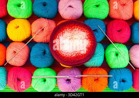 All for hand knitting. Knitted multi-colored handmade fabric with balls of multi-colored threads, pins and various knitting needles on it. Stock Photo