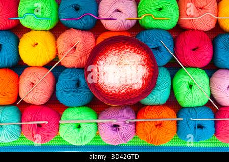 All for hand knitting. Knitted multi-colored handmade fabric with balls of multi-colored threads, pins and various knitting needles on it. Stock Photo