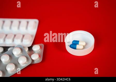 Blister packs with two blue-and-white capsules placed in a plastic lid on vivid red background, clean pharmaceutical flat lay for ads. High quality photo Stock Photo
