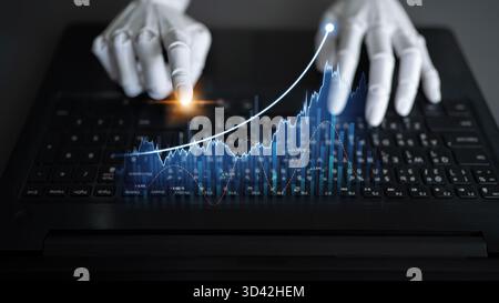 A close-up view of robotic hands operating a laptop keyboard while displaying animated digital financial data, symbolizing innovation in financial Stock Photo