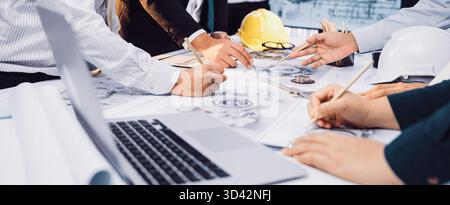 A diverse team of engineers and architects collaborates on project plans in a modern office setting, surrounded by construction tools and documents Stock Photo