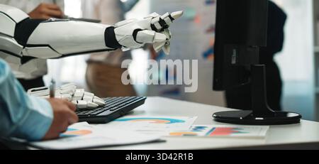 A robotic hand pointing at a computer screen, showcasing business charts and data analysis in a modern office setting, emphasizing automation and Stock Photo