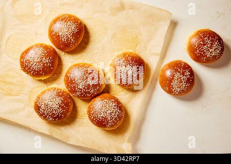 Freshly baked brioche buns with sesame seeds on baking paper. Golden homemade burger buns cooling after baking. Stock Photo