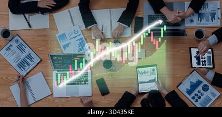 A business team collaborates in a meeting room, analyzing financial data on laptops and tablets, highlighting trends with charts and graphs for Stock Photo