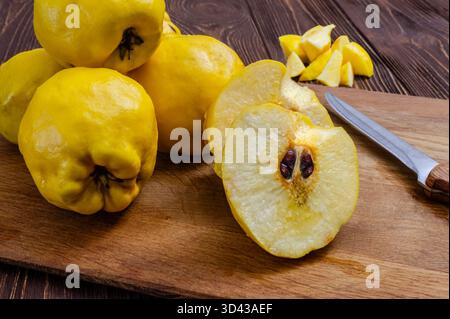Close-up shot of whole and cut ripe yellow quince fruit with seeds visible, resting on a rustic wooden board with a knife. Ideal for food, cooking, he Stock Photo