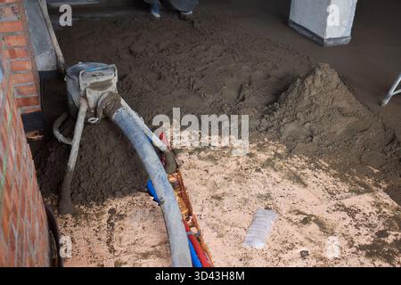 Concrete application process explained, Industrial pump lays concrete on flooring area, Workers use pump equipment to apply concrete onto indoor Stock Photo