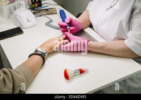 Food, Close-up of a professional performing a manicure using an electric nail file on a client's hand at a beauty salon Stock Photo