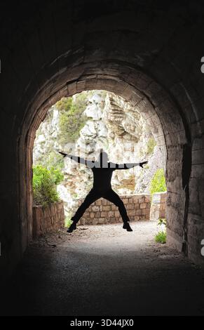 Silhouette of a man jumping in a dark tunnel on the walking path in Petrovac bay, Montenegro Stock Photo