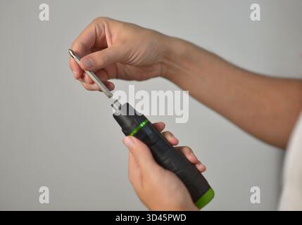 Close-up of hands inserting a metal bit into an electric screwdriver. DIY repair, construction, handyman, and tool maintenance concept on neutral back Stock Photo