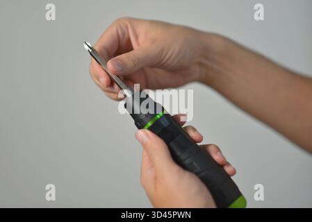 Close-up of hands inserting a metal bit into an electric screwdriver. DIY repair, construction, handyman, and tool maintenance concept on neutral back Stock Photo