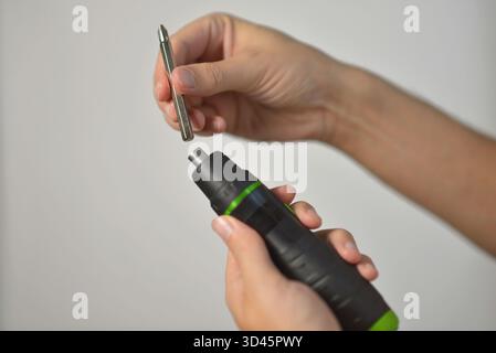 Close-up of hands inserting a metal bit into an electric screwdriver. DIY repair, construction, handyman, and tool maintenance concept on neutral back Stock Photo