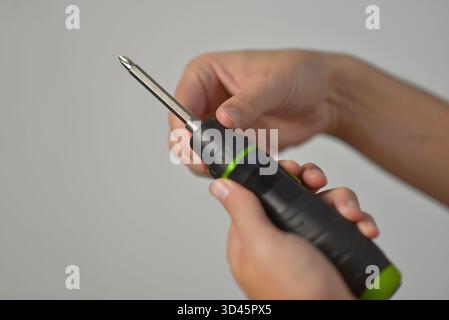 Close-up of hands inserting a metal bit into an electric screwdriver. DIY repair, construction, handyman, and tool maintenance concept on neutral back Stock Photo