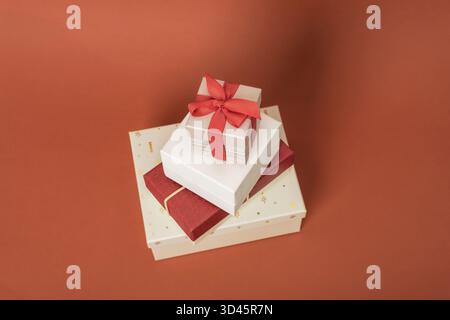 Stack of gift boxes with red ribbon bows on brown background. Christmas holiday concept. Stock Photo