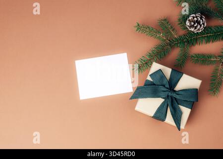 Blank card, gift box and fir branch on brown background. Merry Christmas greeting card. Top view, flat lay, mockup. Stock Photo