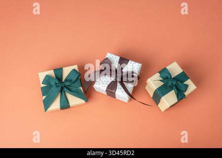 Three gift boxes with green and brown bow on orange background. Top view, flat lay. Stock Photo