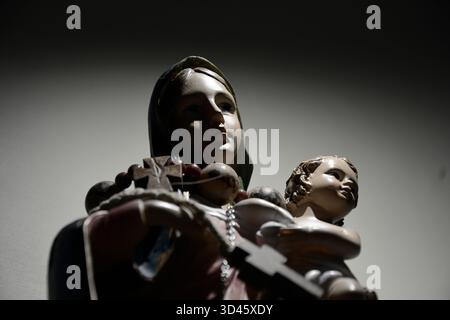 Low angle shot of a Blessed Virgin Mary and Baby Jesus statue, with a small wooden bracelet around the neck. Harsh lighting. Stock Photo