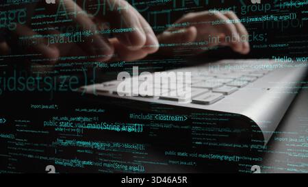 Close-up view of hands typing on a laptop keyboard, immersed in green code and programming text, illustrating the dynamic world of software Stock Photo