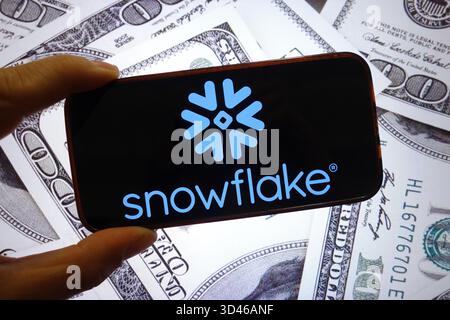 In this photo illustration, the Snowflake company logo is seen displayed on a smartphone screen with United States dollar banknotes in the background. Stock Photo