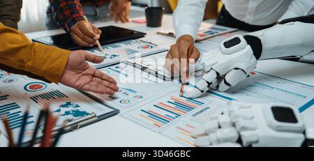 A dynamic meeting scene showing human and robot hands engaging with data charts on a conference table, symbolizing the future of collaboration and Stock Photo