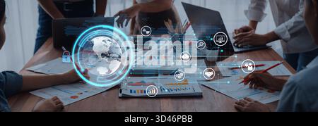 A dynamic business meeting with professionals collaborating around laptops and tables, featuring digital data visualization tools and global analytics Stock Photo