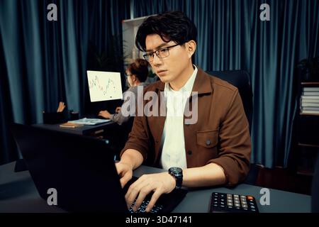 Serious face of thinking businessman focusing laptop to report data analysis social media online project with coworker analyzing stock at back side at Stock Photo