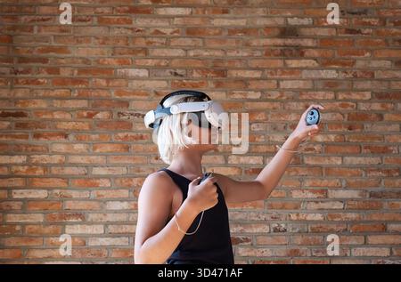 Boy with virtual reality headset playing, holding controllers. Teenager exploring VR game or educational simulation. Future technology. Stock Photo