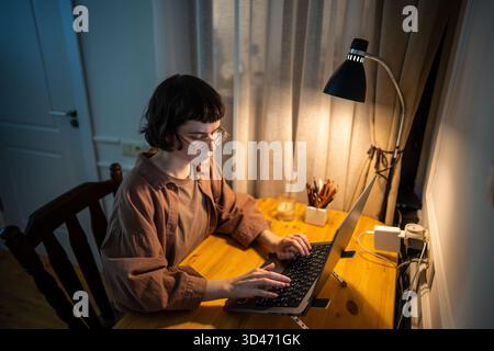 Young business woman freelancer working late at night on laptop, finishing projects, typing reports. Stock Photo