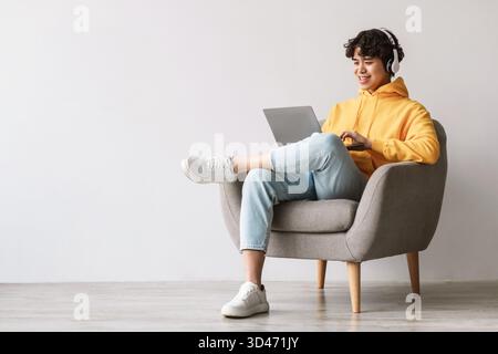 Young Asian Man Enjoys Online Work While Sitting Comfortably in an Armchair Stock Photo