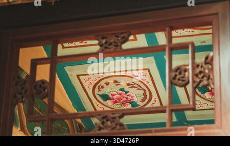 Intricate details of traditional Chinese architecture: A carved wooden window frames a vibrant, painted ceiling from Beijing, China. Stock Photo