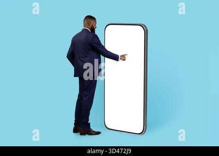 Curious Black Businessman Standing Near Huge Blank Smartphone And Touching White Screen Stock Photo