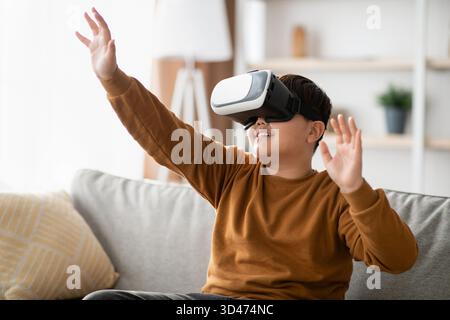 Excited Chubby Teen Boy Using VR Glasses and Interacting With Virtual Reality at Home Stock Photo