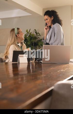 Collaborating Diverse female colleagues working at table in home office, with laptop and microphone Stock Photo
