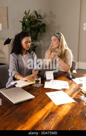 Collaborating Diverse female colleagues reviewing charts at office desk with notebook and tablet Stock Photo
