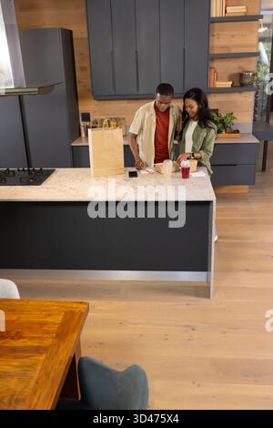 African American male friends unpacking paper bag and takeaway boxes on kitchen island, with drink Stock Photo