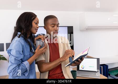 Collaborating African American male coworkers reviewing notebook with stylus at desk in office Stock Photo